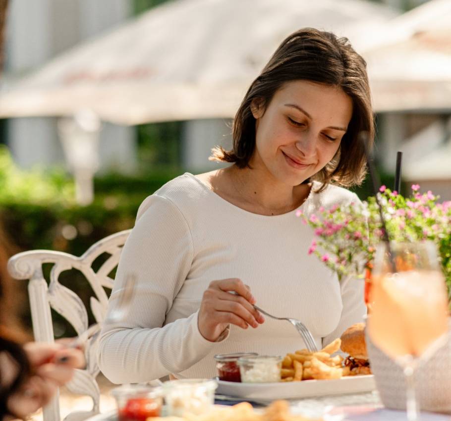 A woman enjoys lunch with fries, a burger, and a drink outdoors in the sunshine on the island of Rügen.