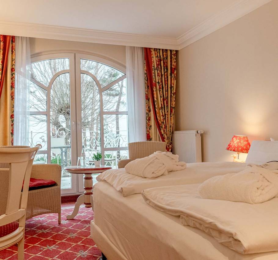Doppelzimmer mit gemütlichem Doppelbett, Balkonblick und floralen Vorhängen im Rugard Thermal Strandhotel Binz