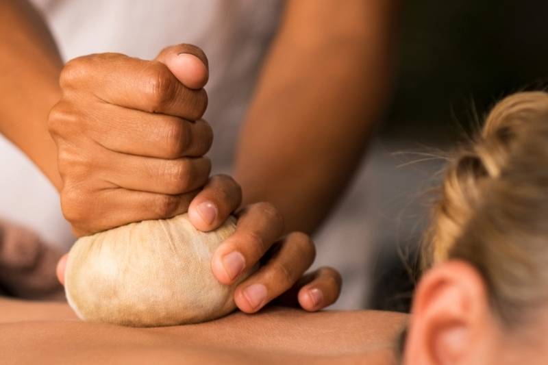 Nahaufnahme einer Frau bei einer wohltuenden ayurvedischen Kräuterstempelmassage auf dem Rücken.