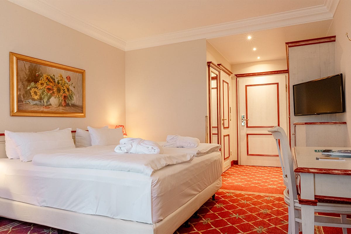 Double room with a large bed, desk, wall painting, and warm colors at Rugard Thermal Strandhotel