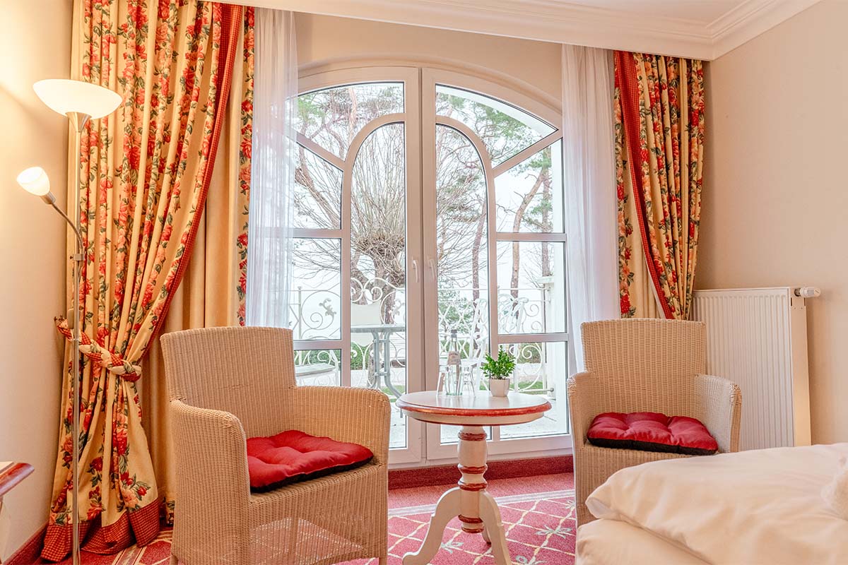 Elegant seating area with rattan chairs, table, and balcony view of nature at Rugard Thermal Strandhotel