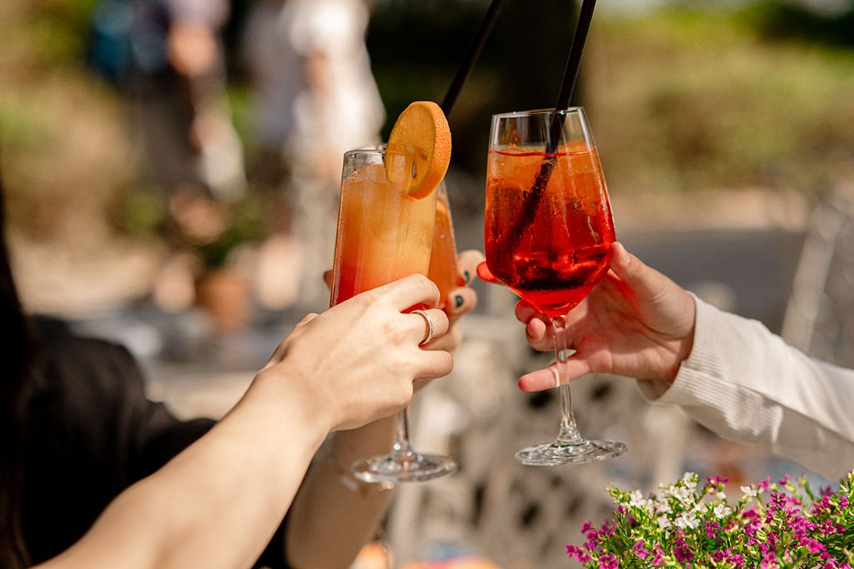 Drei Personen, von denen man nur ihre Hände sieht, stoßen mit Cocktails im Restaurant in Binz an.