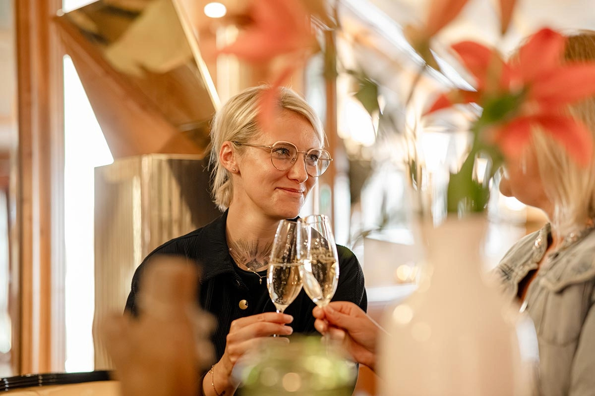 Zwei Frauen stoßen mit einem Glas Champagner an.