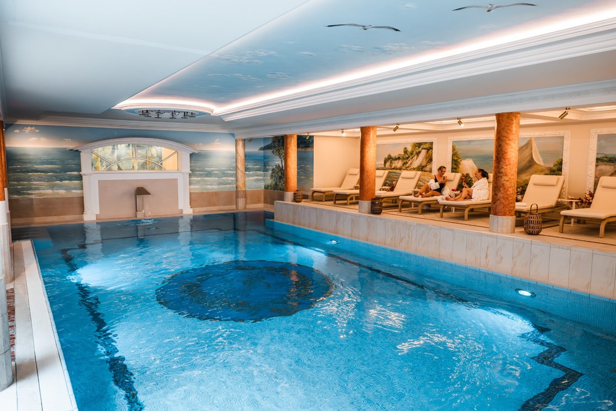 Gäste entspannen im blauen Pool mit weiß-kupferfarbenen Säulen im Hintergrund im Hotel mit Sauna in Binz auf Rügen.