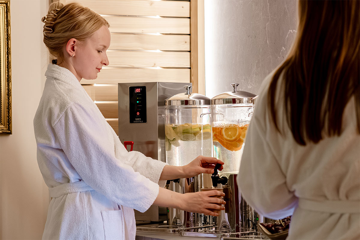 Woman in a bathrobe taps fresh Rügen water with citrus fruits at the spa bar of the Rugard Thermal Strandhotel.