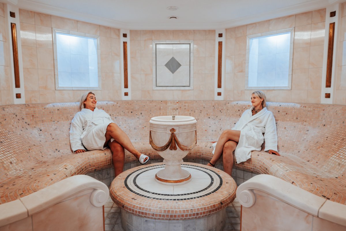 Two women sit in the caldarium of the Rugard Strandhotel on heated stone benches with mosaic cladding