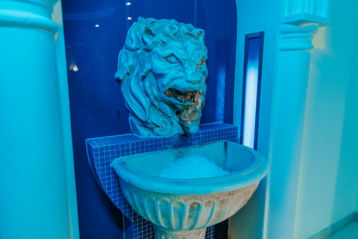 Lion's head with ice fountain under blue lighting, part of the wellness area in the Rugard Thermal Strandhotel.