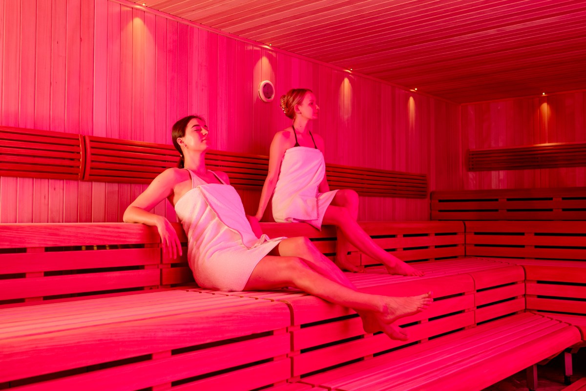 Two women sit in the red-lit Finnish sauna at the Rugard Thermal Strandhotel.