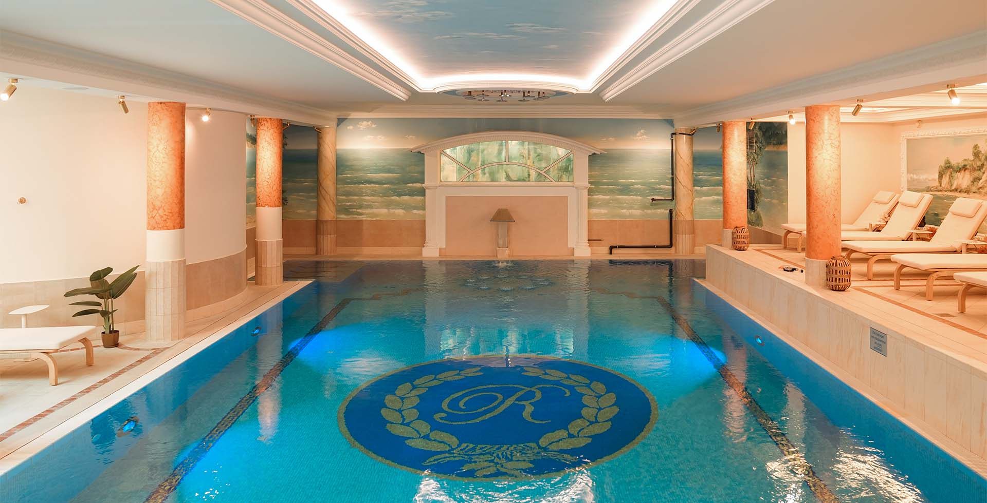 Bright indoor pool with mosaic floor, columns and murals in the wellness area of the Rugard Thermal Strandhotel on Rügen.