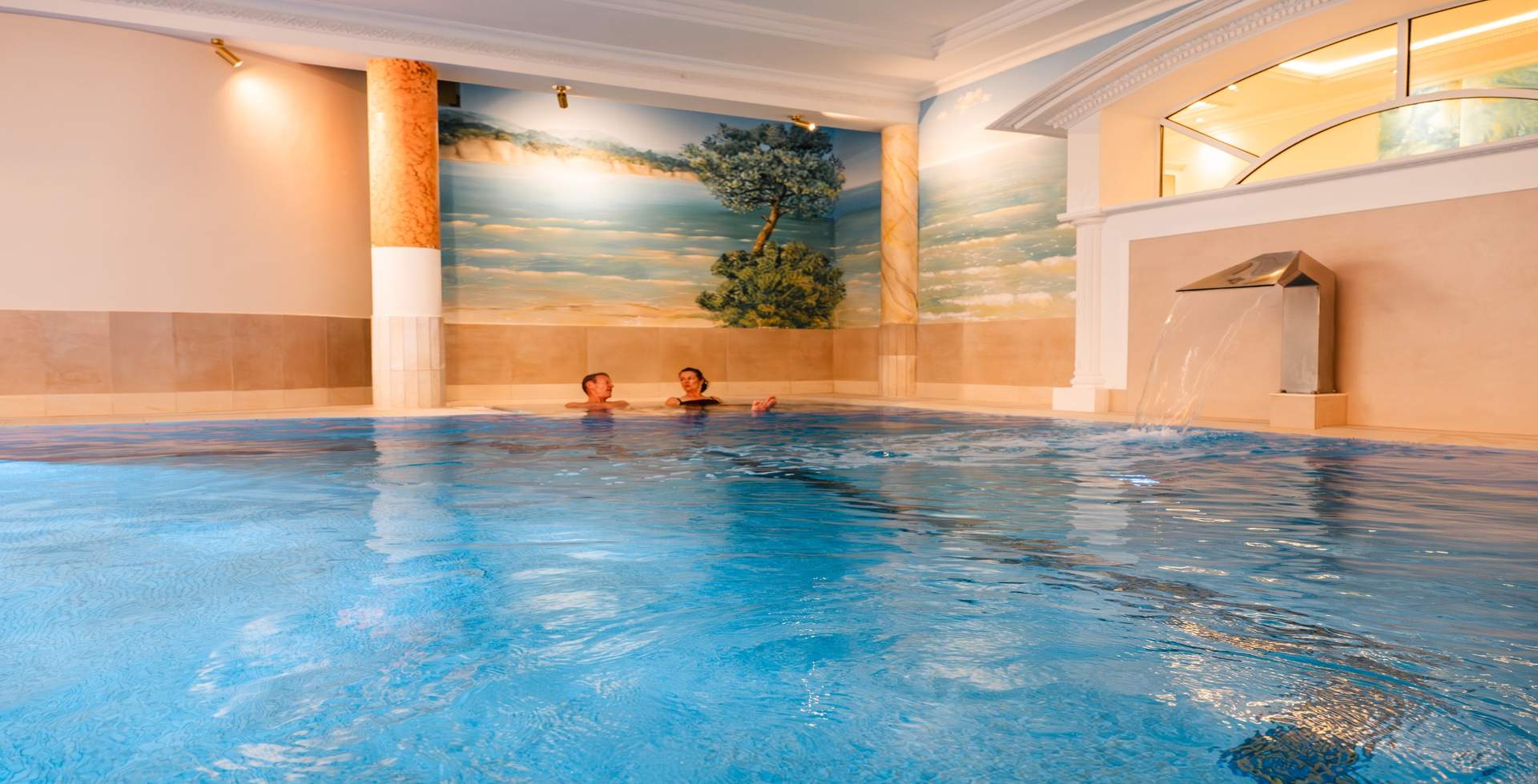 Frau entspannt im Wellnesspool mit Wasserfall im Spa-Bereich des Rugard Thermal Strandhotels in Binz.